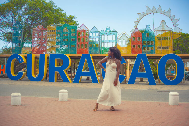 Woman in a white dress walking in front of the colorful CURACAO sign