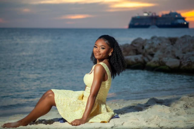 Woman in a yellow dress sitting on rocks by the water with cruise ships in the background in Curacao