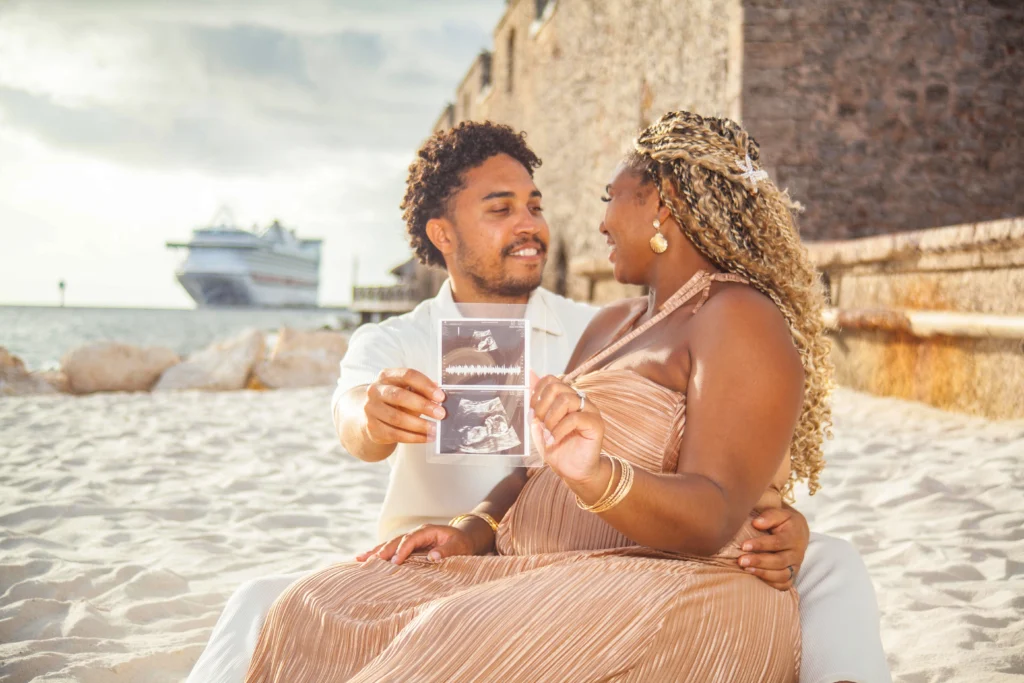 Couple sitting on the beach holding a photo, with a cruise ship in the background in Curacao