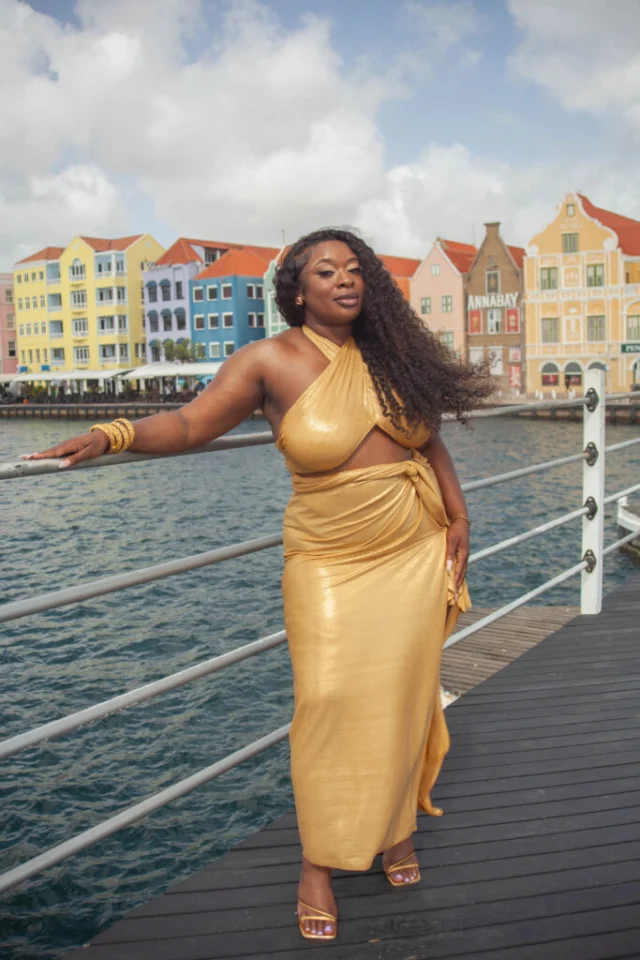 Woman in a gold dress on the Queen Emma pontoon bridge with Willemstad's waterfront in the background