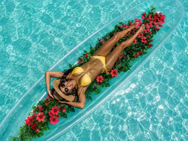 Woman posing on a flower-decorated clear kayak in turquoise Curacao water